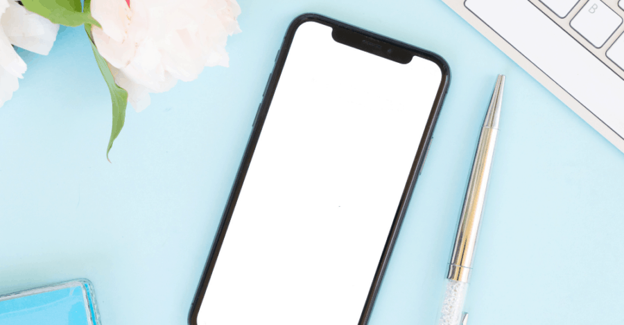 Flat lay of a mobile phone, pen and flowers on a light blue background