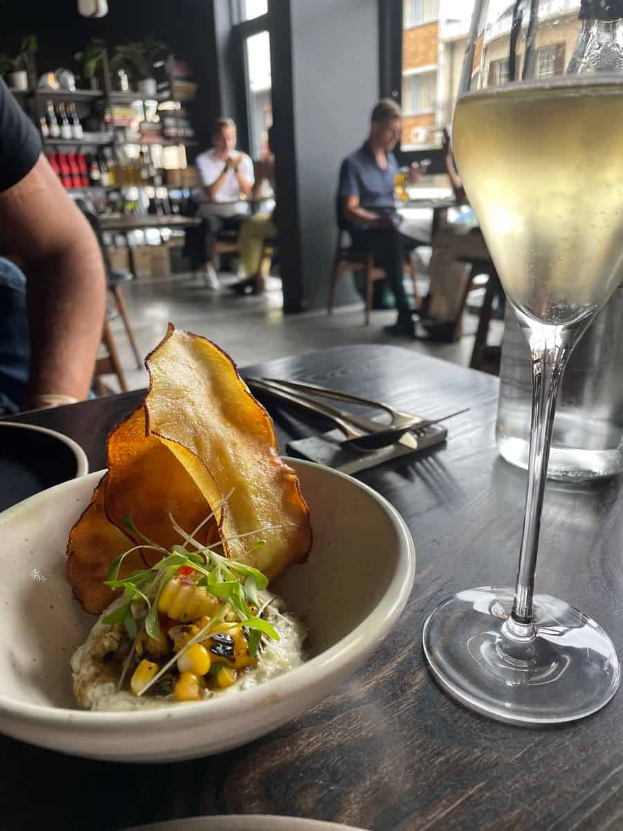 A bowl with sweet potato crisps and snoek pate with a glass of sparkling wine